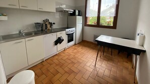 Cocina compacta con armarios blancos, una estufa y un ventanal con vistas a la vegetación.
