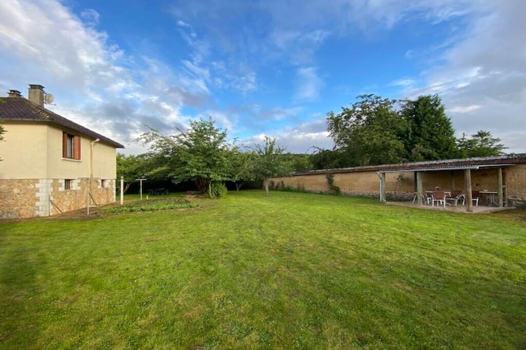 A spacious backyard with a well-maintained lawn, a stone wall, and a small patio area with outdoor seating.