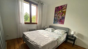 Un dormitorio con cama, una mesita de noche, una ventana con cortinas y un cuadro en la pared.