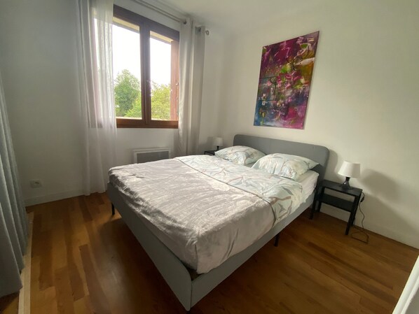A bedroom with a bed, a nightstand, a window with curtains, and a painting on the wall.