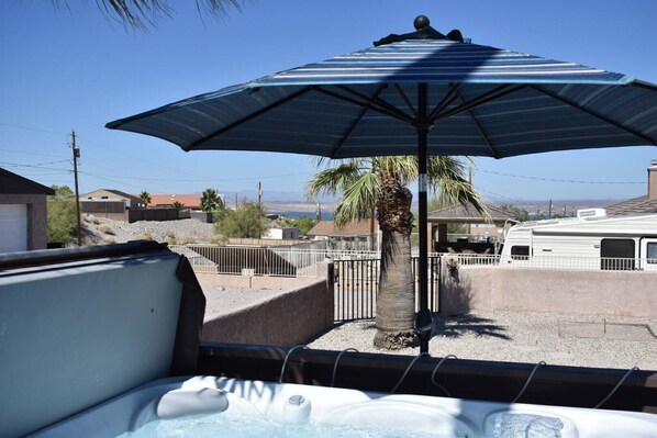 Un jacuzzi con sombrilla, una palmera y una autocaravana en un barrio residencial.
