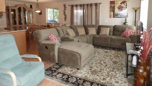A living room with a sectional sofa, a blue armchair, a patterned rug, and a dining area in the background. - Cisco Surprise with a SPA (Lake Havasu City)