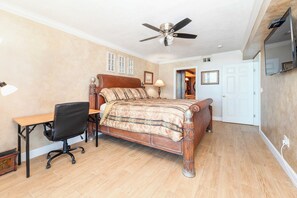 Une chambre à coucher comprenant un lit, un bureau, une chaise, un ventilateur de plafond et un téléviseur fixé au mur.