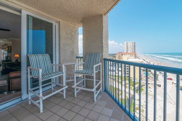 Un balcon avec deux chaises à rayures et une table, donnant sur une plage et un immeuble de grande hauteur.