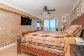 A bedroom with a large bed, a ceiling fan, a TV, and a balcony with a view.