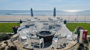 Un espace extérieur circulaire aménagé avec des chaises et un foyer, offrant une vue sur la plage.