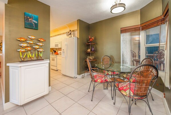 Comedor con mesa de vidrio y sillas de mimbre, cocina al fondo y una pieza decorativa de arte mural con peces.