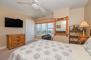 Un dormitorio con cama, televisión, ventilador de techo, ventana con vistas, cómoda y lámpara.