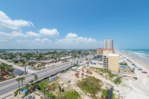 A coastal cityscape with a beach, a highway, and a large hotel with multiple floors. - 10th Floor Heaven at 1001 Towers 10 3/3 Oceanfront (Daytona Beach Shores)