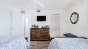 Un dormitorio con dos camas, un tocador, un televisor, un espejo y una puerta que da a otra habitación.