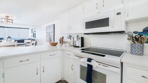 A modern kitchen with white cabinetry, a built-in microwave, and a coffee maker.