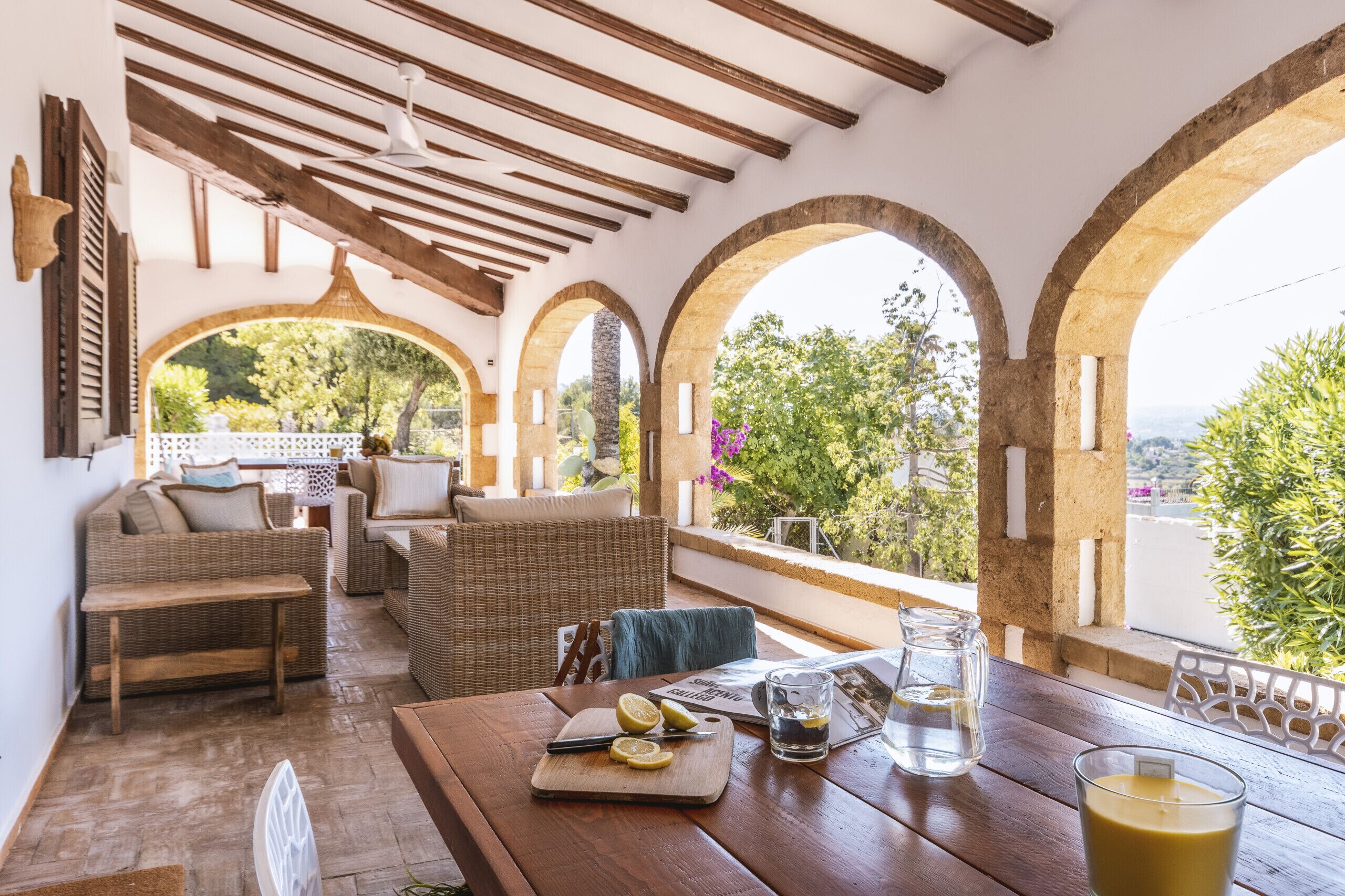 Un espacio exterior acogedor con mobiliario de mimbre, una mesa de madera con una tabla de cortar y limones, y un vaso de bebida.