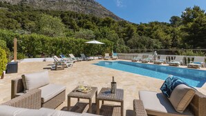 Ein Poolbereich mit Liegestühlen, einem Tisch mit Getränken und Blick auf eine Berglandschaft.