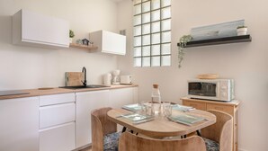 Une cuisine moderne avec des meubles blancs, une table à manger avec des chaises, un four à micro-ondes et une fenêtre donnant sur la mer.