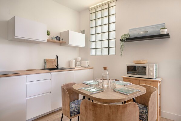 Uma cozinha moderna com armários brancos, uma mesa de jantar com cadeiras, um micro-ondas e uma janela com vista para o mar.