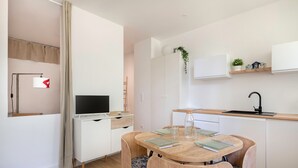 Une cuisine moderne avec des meubles blancs, une table à manger en bois et un téléviseur encastré.