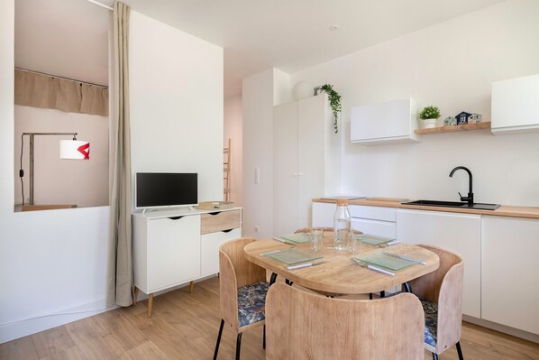 Una cocina moderna con armarios blancos, una mesa de comedor de madera y un televisor empotrado.