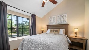 Une chambre à coucher avec un grand lit, deux lampes de chevet, un ventilateur de plafond et une fenêtre avec des rideaux.