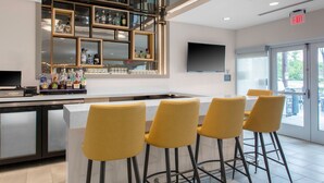 A bar area with stools, a counter with bottles, and a TV mounted on the wall. - TownePlace Suites by Marriott Dayton Wilmington (Wilmington)