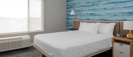 Habitación de hotel con una cama grande, una mesita de noche, una lámpara, un calentador y vistas a la ciudad a través de una ventana.