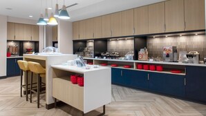 A modern kitchen with wooden cabinets, a central island with stools, and various kitchen appliances. - TownePlace Suites by Marriott Dayton Wilmington (Wilmington)
