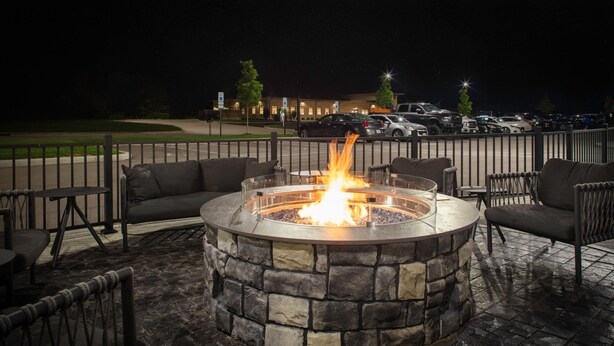 An outdoor seating area with a stone fire pit surrounded by chairs and tables. - TownePlace Suites by Marriott Dayton Wilmington (Wilmington)