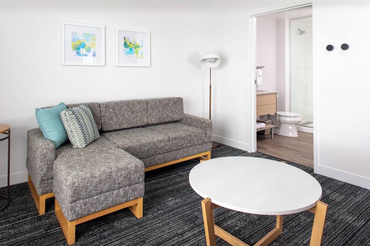 Una sala de estar moderna con un sofá seccional gris, una mesa redonda blanca y una lámpara de pie.