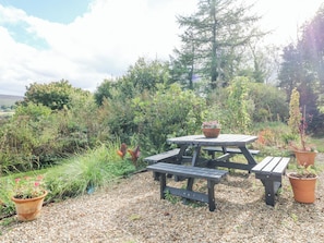 A picnic table with a bench, surrounded by gravel and potted plants.