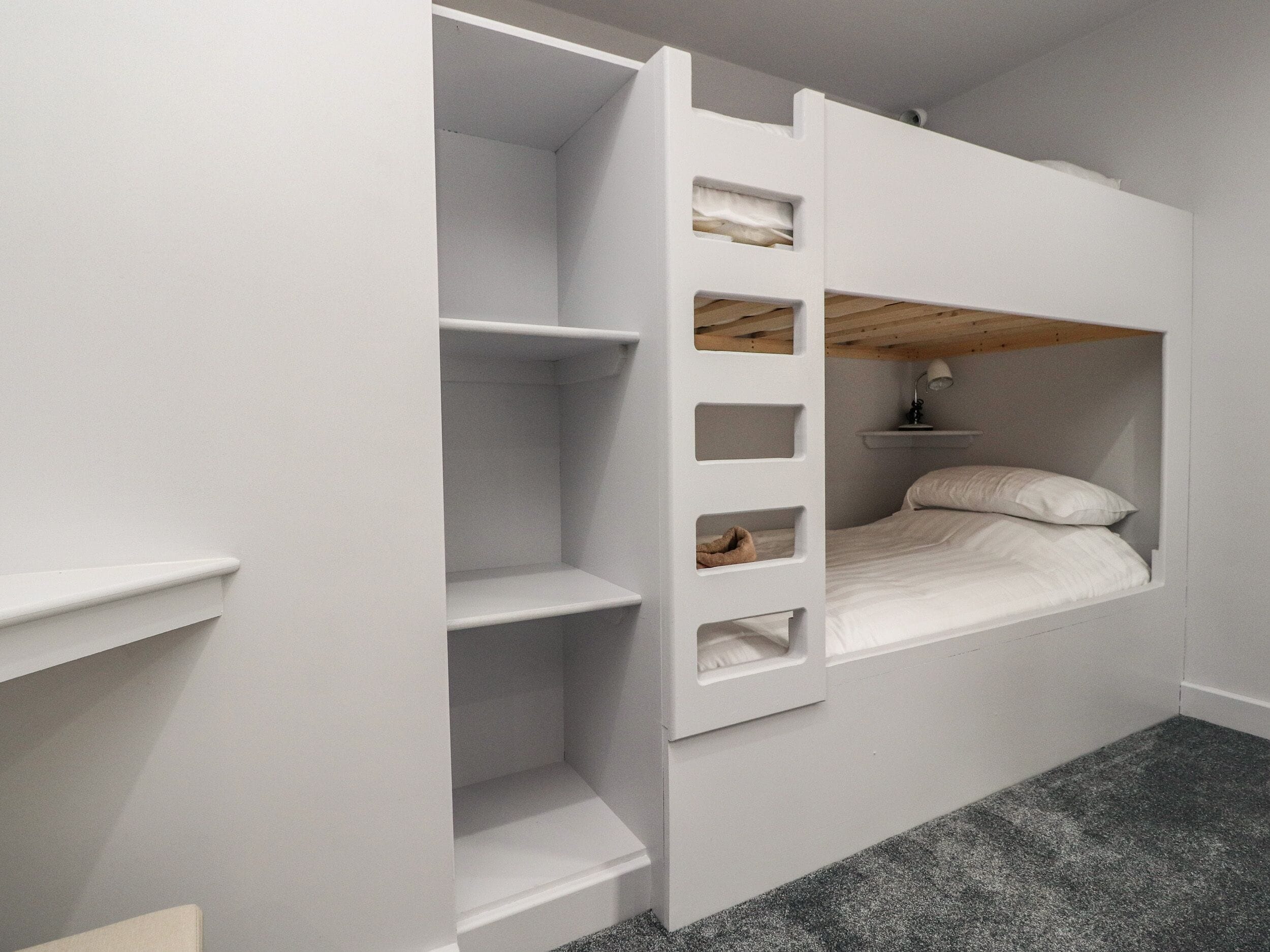 A bunk bed with built-in shelving, a desk, and a lamp.