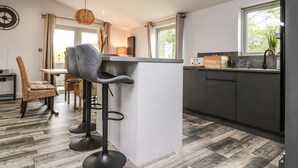 Et moderne køkken med bar, trægulv og spiseplads med fletstole.