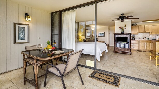 A dining area with a table and chairs, a bed with a view, a kitchen with cabinets and appliances, and a ceiling fan.