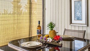 A dining table with a glass top, a bottle of wine, a pineapple, and a fruit basket.
