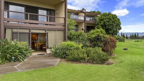 A multi-story residential building with a balcony, a well-maintained lawn, and a clear sky.