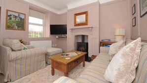A living room with a fireplace, striped sofas, a coffee table, and a television. - Tor View @ Fourwinds (Okehampton)
