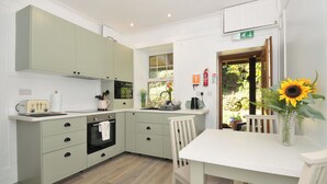A kitchen with light green cabinets, a white countertop, a vintage toaster, and a table with a vase of sunflowers. - Tor View @ Fourwinds (Okehampton)