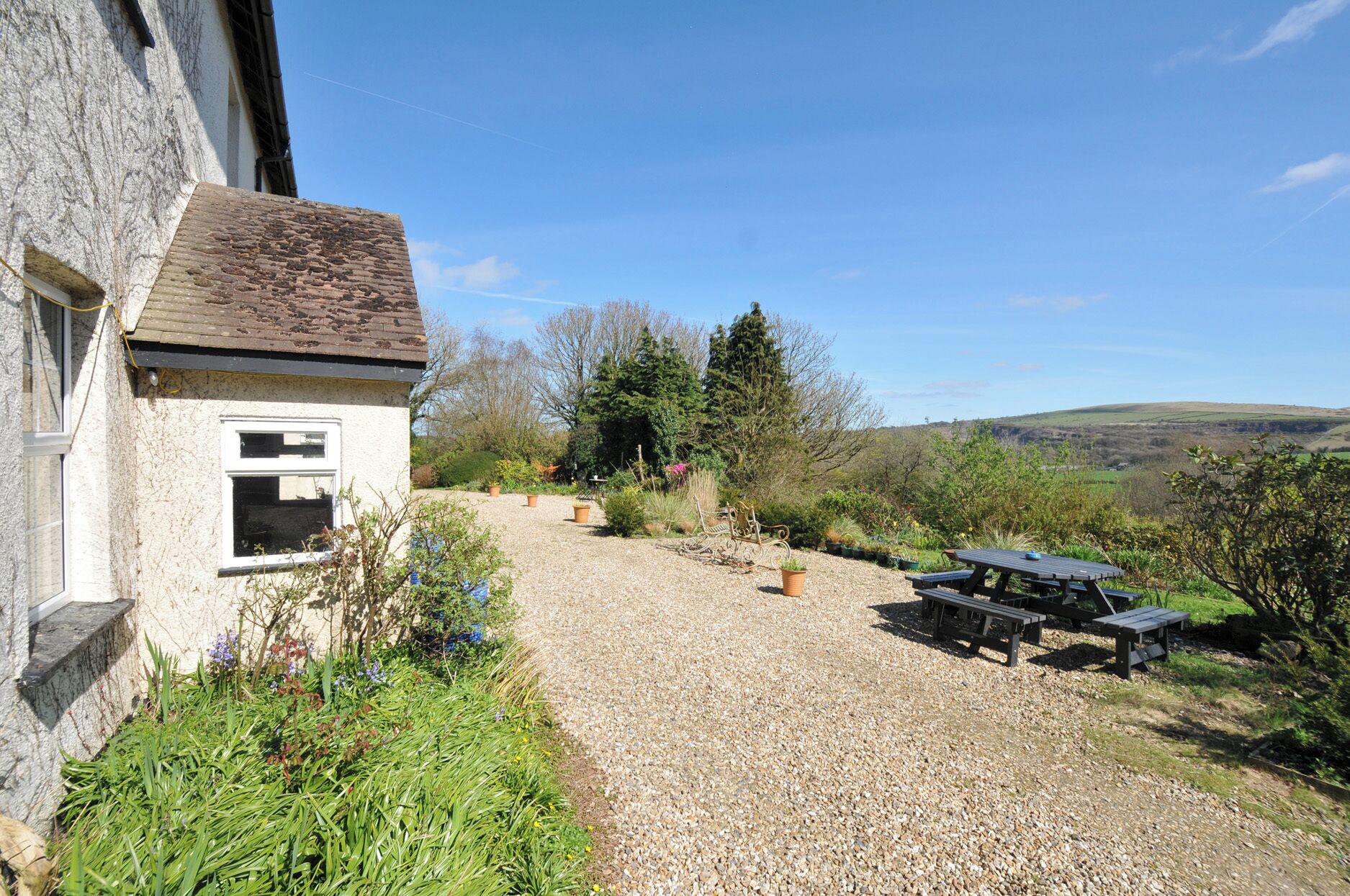 A gravel path leading to a house with a garden, a picnic table, and a bench.