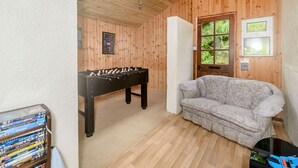A cozy room with a foosball table, a sofa, and a window with a view of greenery. - Tor View @ Fourwinds (Okehampton)