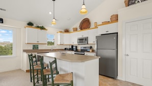 A modern kitchen with a large island, white cabinetry, and a stainless steel refrigerator. - The Hidden Gem: Hot Tub, Private Pool, Currituck Club Amenities (Corolla)