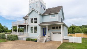 A two-story house with a blue exterior, a front porch, a garage, and a small front yard. - The Hidden Gem: Hot Tub, Private Pool, Currituck Club Amenities (Corolla)