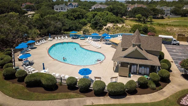 A swimming pool with lounge chairs and umbrellas, surrounded by well-maintained bushes and a building with a pitched roof. - The Hidden Gem: Hot Tub, Private Pool, Currituck Club Amenities (Corolla)