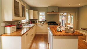Una cocina con encimeras de madera, armarios blancos, horno empotrado y una ventana que deja entrar luz natural.