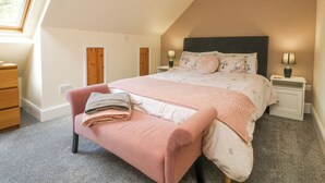 Un dormitorio con cama, mesitas de noche, un banco y una ventana.