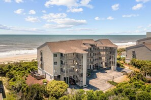 A multi-story building with a beach view, a parking area, and a landscaped garden. - Point Prospect Shores- Ocean Front Condo (Pine Knoll Shores)