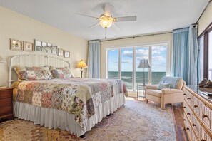 A bedroom with a large bed, a chair, a desk, and a view of the ocean. - Point Prospect Shores- Ocean Front Condo (Pine Knoll Shores)