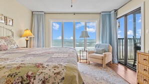 Een slaapkamer met een groot bed, een stoel, een dressoir en uitzicht op de oceaan.