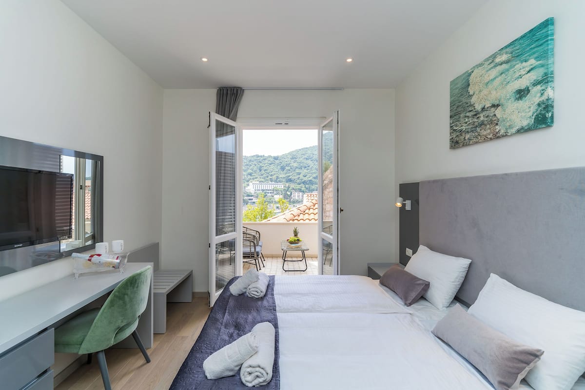 A modern hotel room with a bed, a desk, a chair, and a balcony with a view of the city.