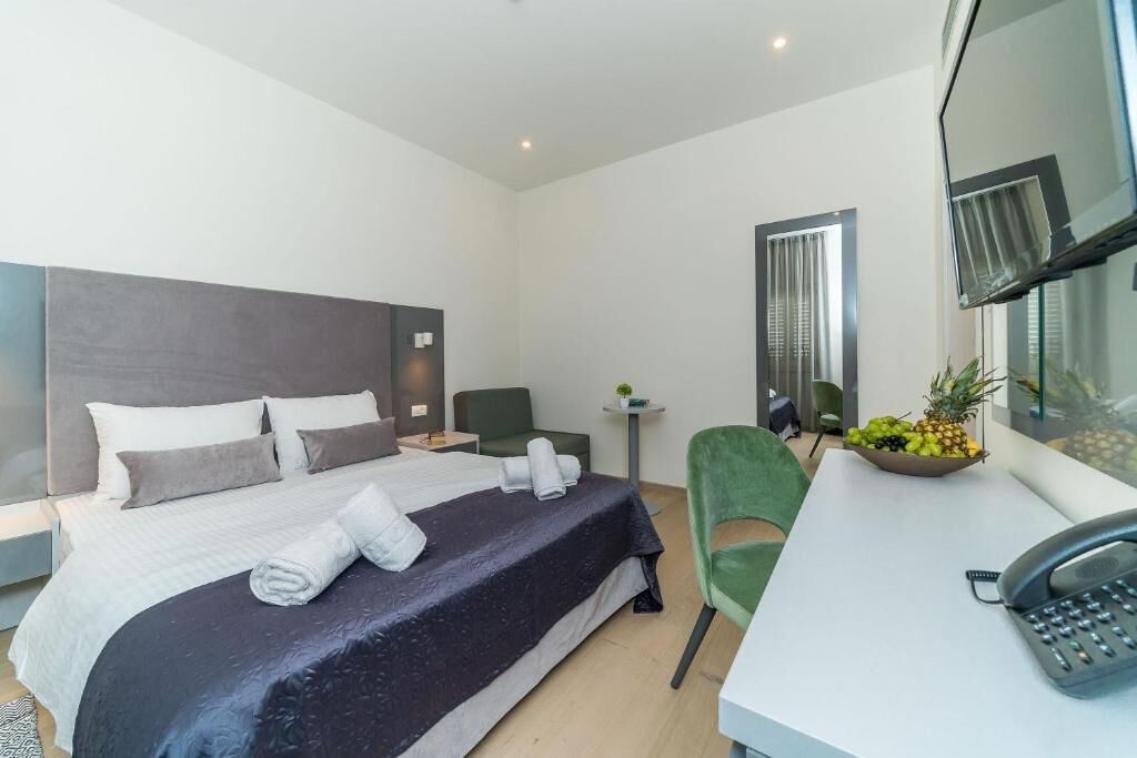Una habitación de hotel moderna con una cama grande, un escritorio con teléfono, una silla verde y un frutero sobre el escritorio.