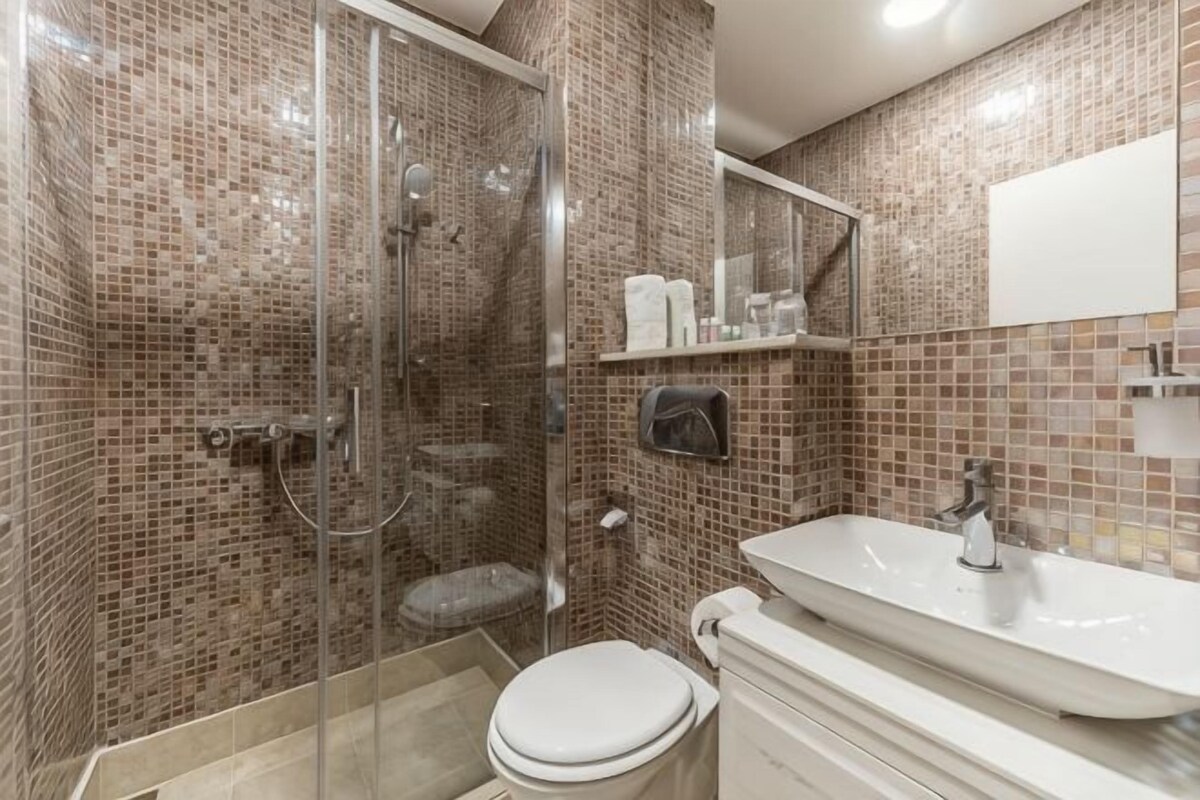 A bathroom with a glass shower enclosure, a toilet, a sink, and a mirror.