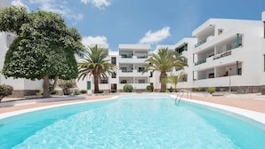 Une piscine entourée de bâtiments blancs dotés de balcons, de palmiers et surplombant un ciel dégagé.