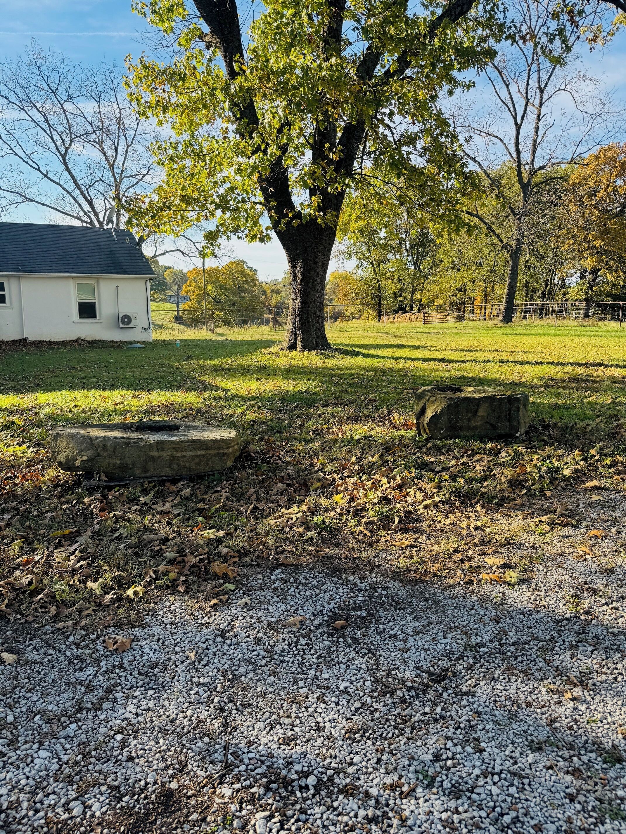 A gravel path leading to a white building with a black roof, surrounded by trees and a grassy field.